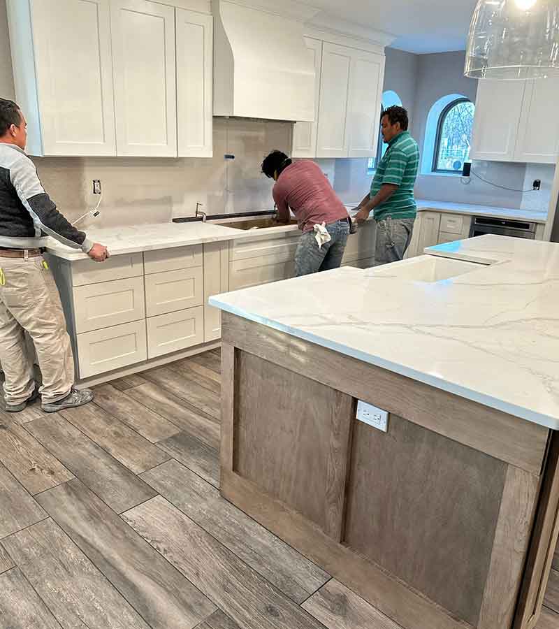 Kitchen island with a white and grey granite waterfall edge, tan cabinets and a skink