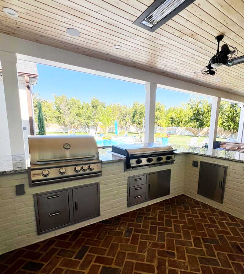 Outdoor kitchen with steel cabinets in brick, a grill and rangetop and brick floor